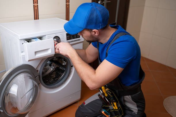 Worker repairing washing machine in laundry room.