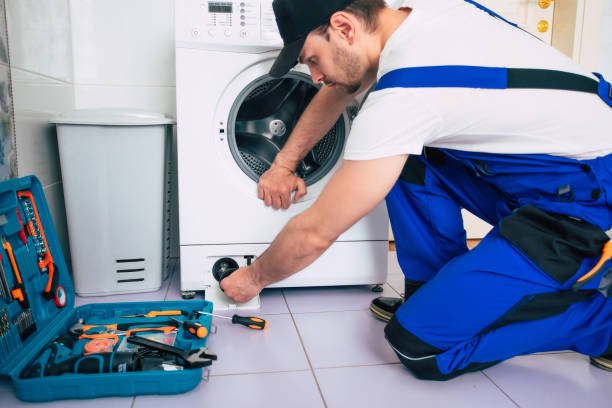 The young handsome repairman in worker suit with the professional tools box is fixing the washing machine in the bathroom